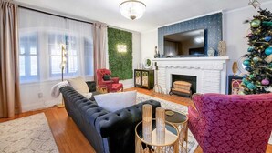 A living room with a black sofa, red chairs, a fireplace, and a Christmas tree. - Clifton Corner: Art Deco charm in College Hill. Walk to the park, dining & shops. 2 king beds. (Wichita)