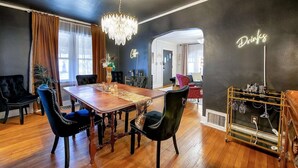 A dining area with a wooden table, upholstered chairs, a chandelier, and a neon sign. - Clifton Corner: Art Deco charm in College Hill. Walk to the park, dining & shops. 2 king beds. (Wichita)