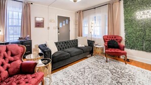 A living room with a black sofa, red armchairs, a patterned rug, and a green wall decoration. - Clifton Corner: Art Deco charm in College Hill. Walk to the park, dining & shops. 2 king beds. (Wichita)