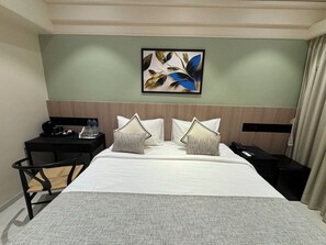 Una habitación de hotel con cama, escritorio, silla, mesita de noche, teléfono y un cuadro en la pared.