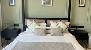 Un lit bien fait, avec du linge de lit blanc et des coussins décoratifs, une table de chevet avec une lampe et un tableau encadré au mur.