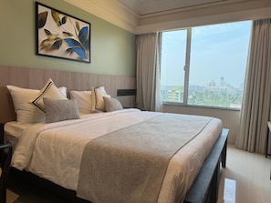 Une chambre d’hôtel avec un grand lit, une vue sur la ville et un tableau accroché au mur.