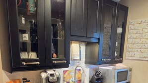 Una cocina con gabinetes oscuros, encimera de granito, cafetera, microondas y un fregadero.