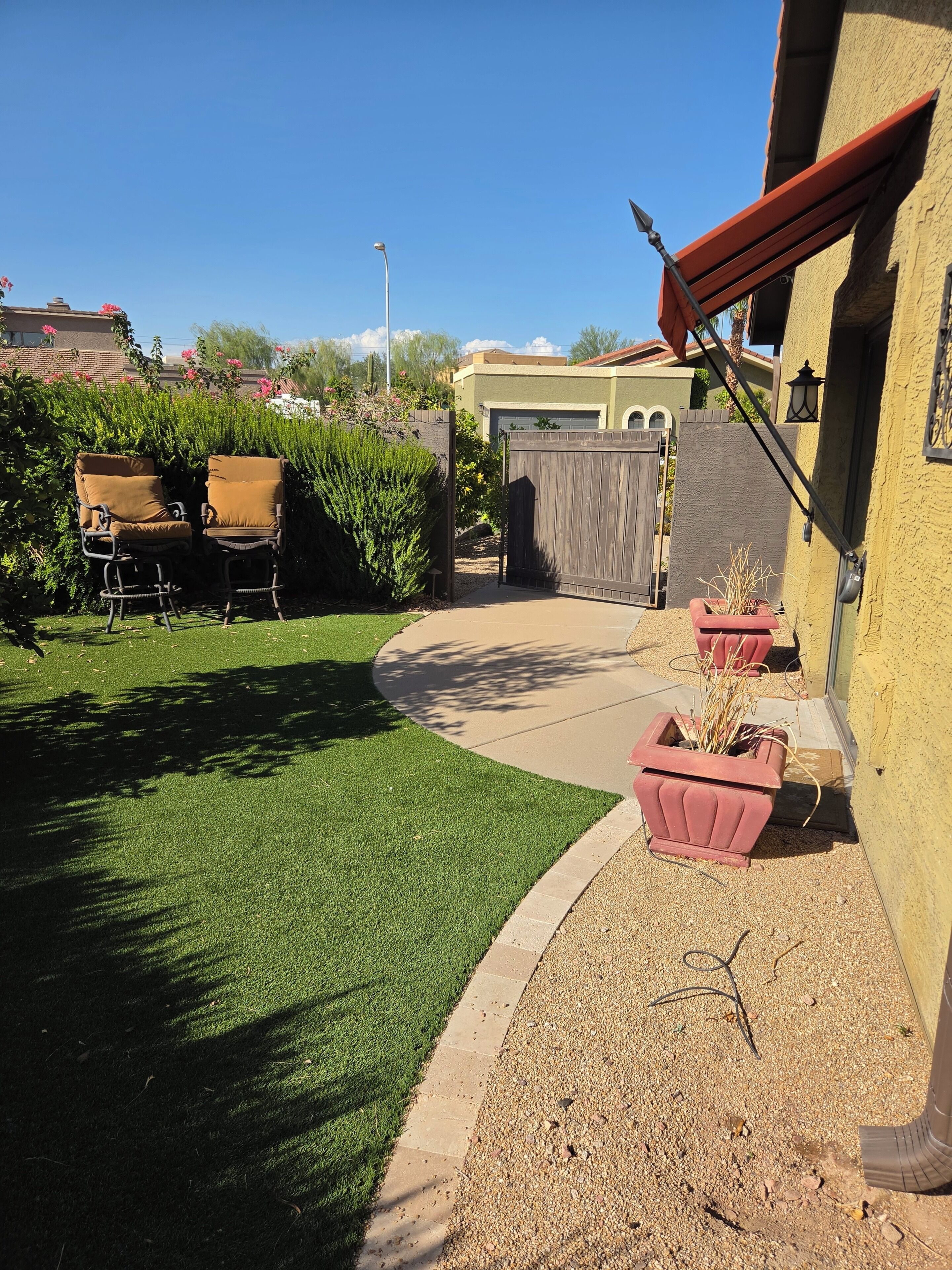 Ein Garten mit künstlichem Rasen, zwei Stühlen, einem Holzzaun und einem Haus mit Garage.