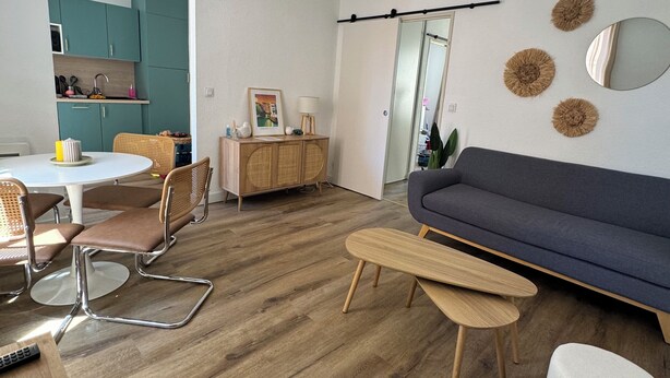 A modern living room with a dark blue sofa, wooden coffee table, and a dining area with teal cabinets and a white table. - Historic center apartment  (Narbonne)