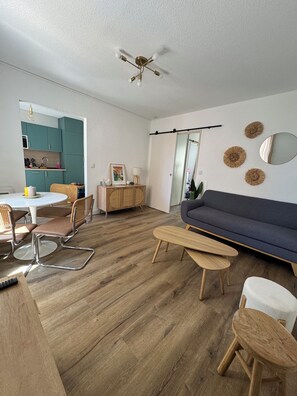 Ein modernes Wohnzimmer mit einem dunkelblauen Sofa, einem Holztisch und einem Essbereich mit türkisfarbenen Schränken und einem weißen Tisch.