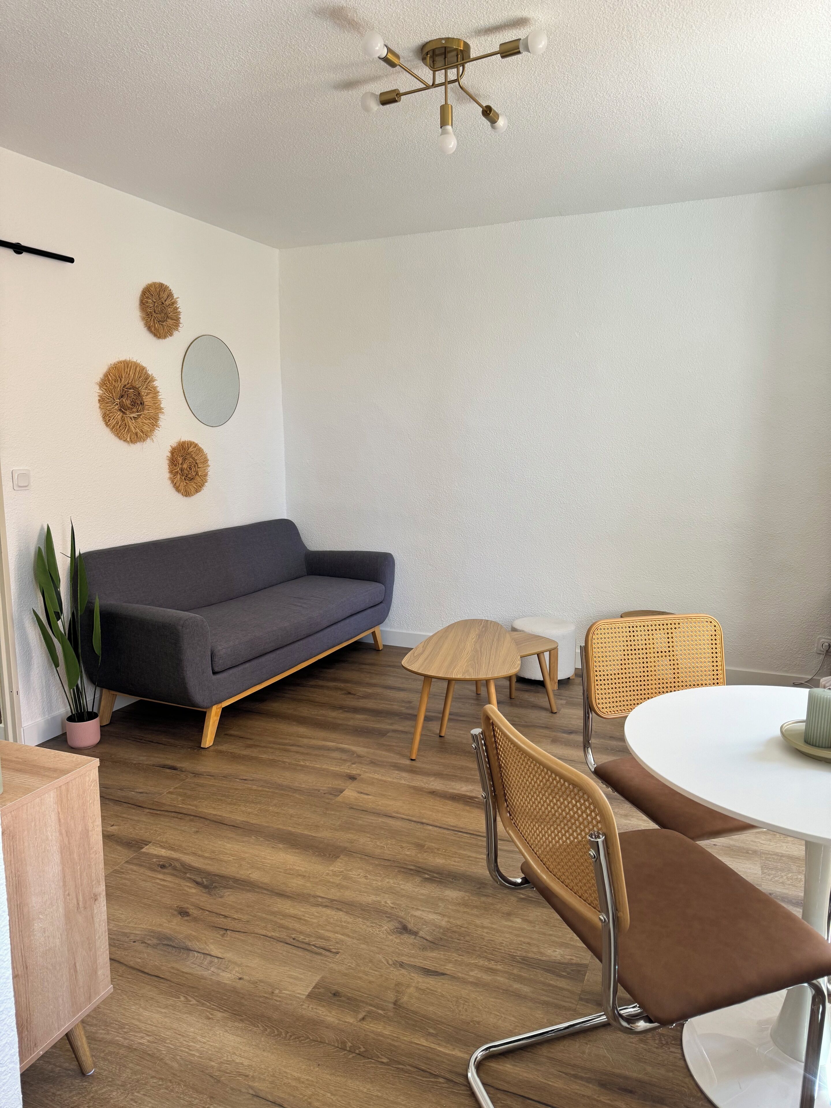 A modern living room with a grey sofa, a round wooden table, and two wicker chairs.