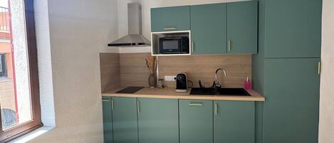 A compact kitchen with teal cabinets, a microwave, and a coffee maker.