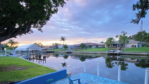 A waterfront property with a dock, a small boat, and a grassy area. - Exclusive Waterfront Retreat Pet Friendly & Dock in the best area of Cape!  (Cape Coral)