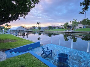 A waterfront property with a dock, a small boat, and a grassy area. - Exclusive Waterfront Retreat Pet Friendly & Dock in the best area of Cape!  (Cape Coral)