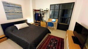 Een slaapkamer met een bed, een bureau, een stoel, een televisie en een kledingkast.