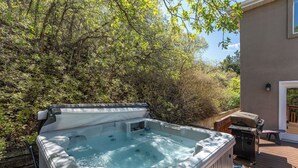 Un jacuzzi en una terraza de madera con una parrilla y una mesa de patio techada.