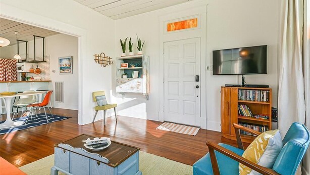 A living room with a wooden floor, a television, a bookshelf, and a door with a decorative sign.