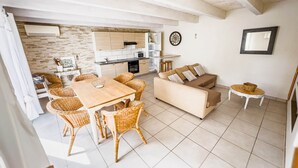 A spacious living area with a dining table, wicker chairs, a sofa, and a small side table. - White Cotton (Elne)