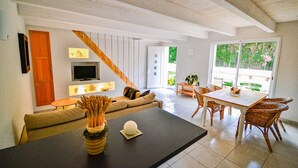 A modern living room with a sofa, a coffee table, a TV, and a dining area with wicker chairs. - White Cotton (Elne)