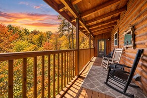 A wooden cabin with a porch, a view of autumn foliage, and a door leading inside.