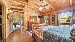 Ein Schlafzimmer in einer Holzhütte mit einem Bett, einem Deckenventilator, einem Fernseher und Blick ins Freie.