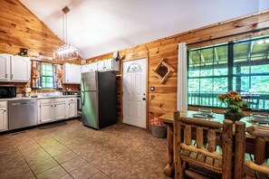 A wooden cabin kitchen with white cabinets, a refrigerator, and a dining table with chairs.