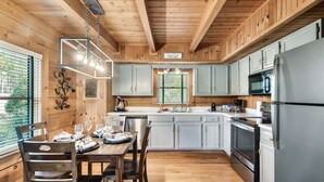 Una cocina de estilo cabaña de madera con una mesa de comedor para cuatro personas, un lavabo, una estufa y un refrigerador.