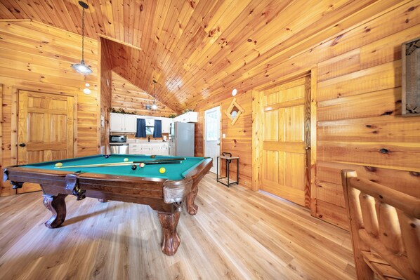 A wooden interior with a pool table, kitchen area, and wooden doors.