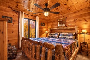 A log cabin bedroom with a bed, a ceiling fan, and a window with autumn foliage view. - Hot Tub with Mountain Views, Fire Pit & Pool Table (Sevierville)