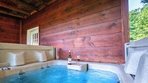 Una vasca idromassaggio con una bottiglia di vino e un bicchiere, pareti in legno e una finestra.
