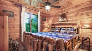 Camera da letto in una baita di legno con un letto, una ventola a soffitto, una finestra e una lampada.