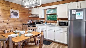 Une cuisine moderne avec des meubles blancs, des appareils en acier inoxydable et une table à manger en bois, accompagnée de chaises.