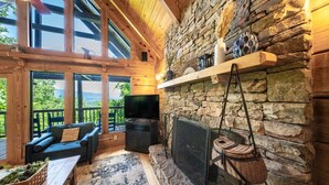 A cozy living room with a stone fireplace, a flat-screen TV, and a comfortable seating area with a view of the outdoors.