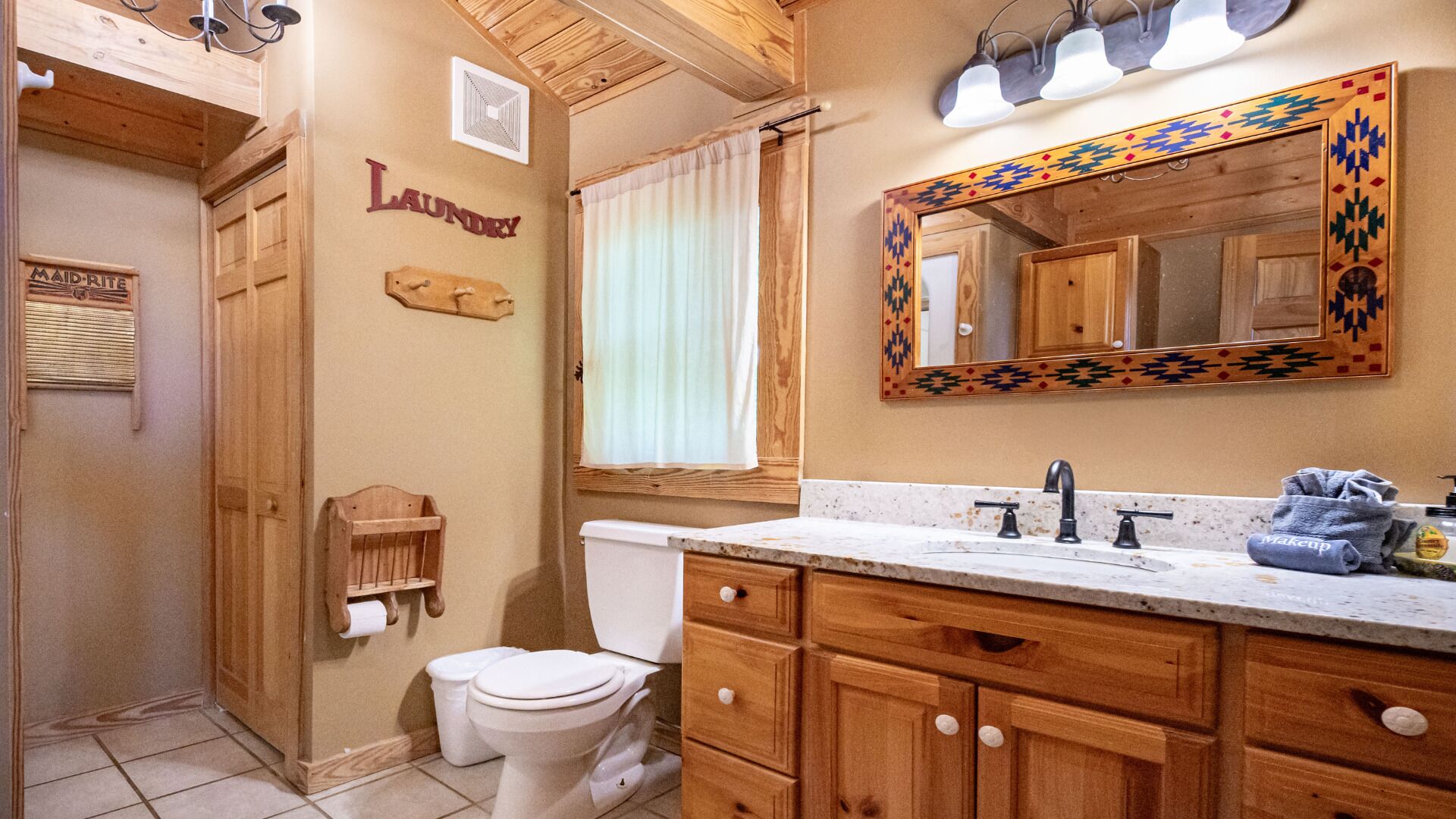 A bathroom with wooden cabinets, a sink, a toilet, and a mirror with a decorative frame.