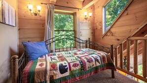 Een slaapkamer in een houten hut met een bed, een raam en uitzicht op bomen.