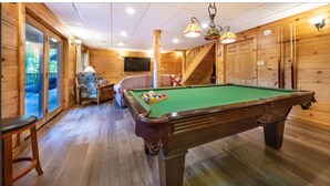 A wooden pool table with a green felt surface, a pool cue rack, and a chair. - Mountain View Cabin with Hot Tub, Fire Pit & Deck (Sevierville)