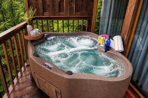 A hot tub on a wooden deck with a wooden railing, surrounded by greenery.
