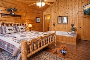 A log cabin bedroom with a bed, a wooden bench, a dog, a bathtub, and a television.