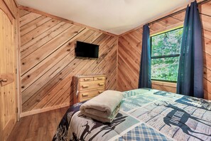 A wooden-paneled room with a bed, a dresser, and a window with curtains. - Mountain-View Cabin · Hot Tub, Fire Pit & Jacuzzi (Sevierville)
