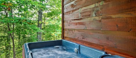 A hot tub with a wooden exterior wall and a view of a forest.