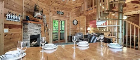 Cozy cabin-style interior with a dining table for four, stone fireplace, and spiral staircase.