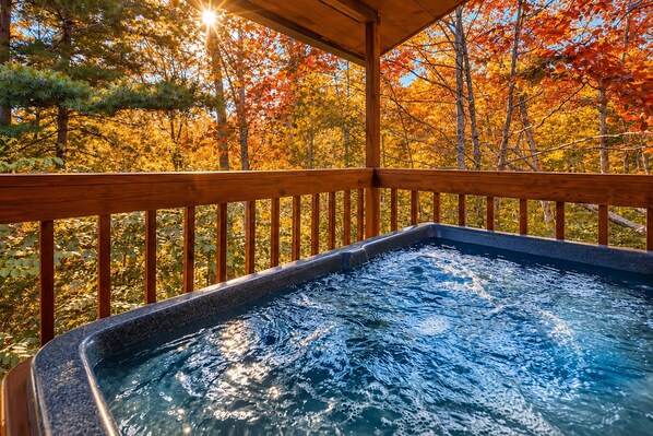 A hot tub with a wooden deck and a view of autumn trees.