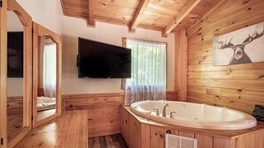 Un bany de cabana de fusta amb una banyera gran, un televisió penjada a la paret i un quadre de cervís.