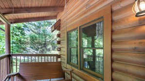 Una cabana de fusta amb un porxo, una banca i grans finestres amb vistes a un bosc.