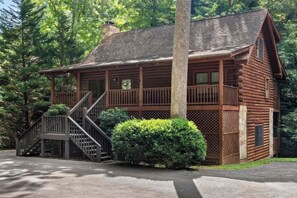 A wooden cabin with a covered porch, a staircase, and a small garden area.