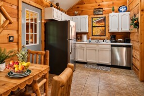 A wooden cabin interior with a dining table, chairs, a black refrigerator, white cabinets, a sink, and a coffee maker. - Smoky Mountain Cabin: Hot Tub & Forest Views (Sevierville)