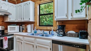 A compact kitchen with white cabinets, a microwave, a coffee maker, and a dishwasher.