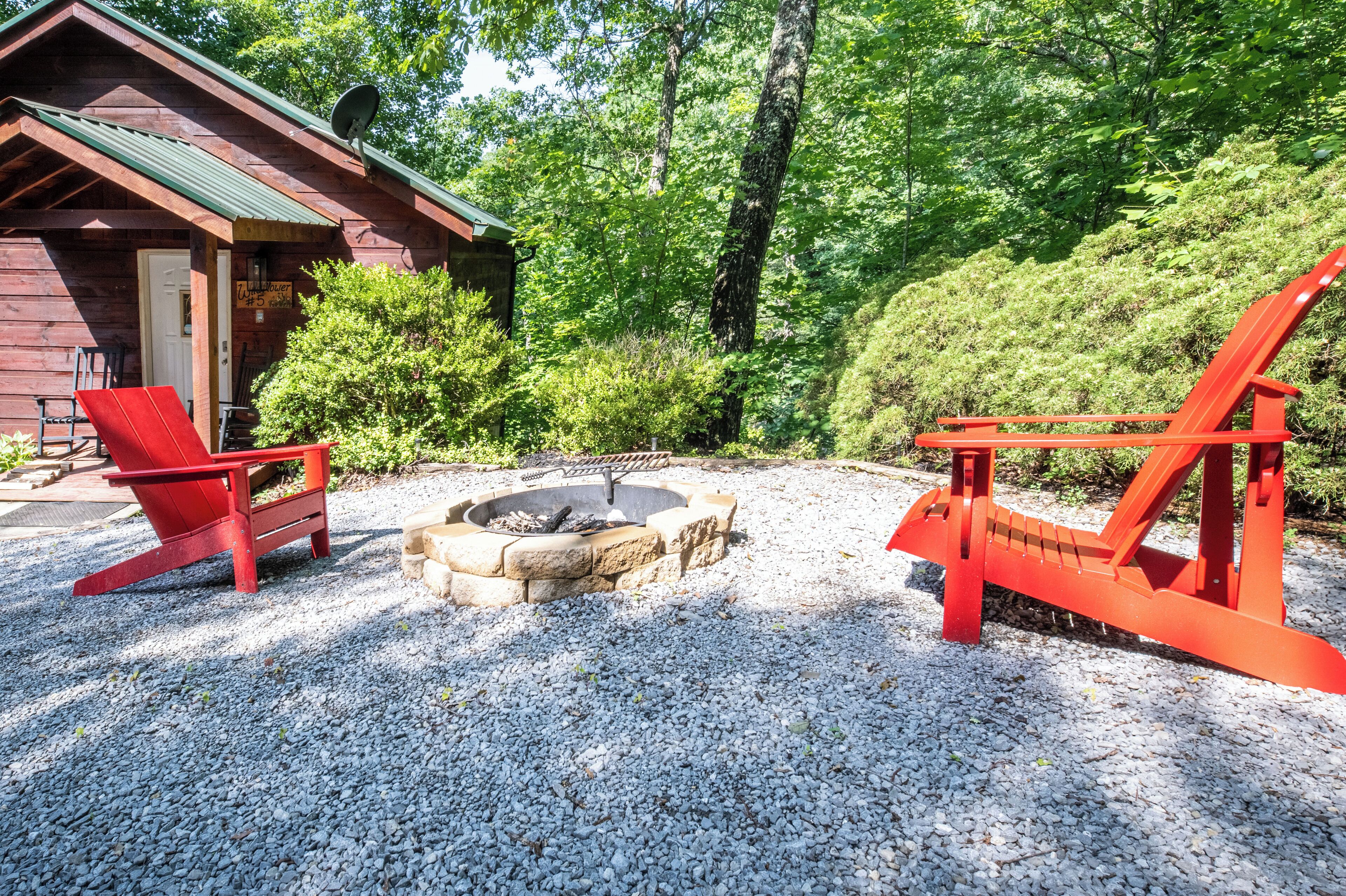 Une cabane avec un foyer et des chaises Adirondack rouges, située dans une zone boisée.