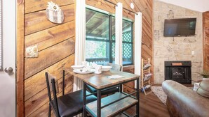 Interior acogedor de una cabaña con una mesa de madera, sillas, chimenea y televisor montado en una pared de piedra.