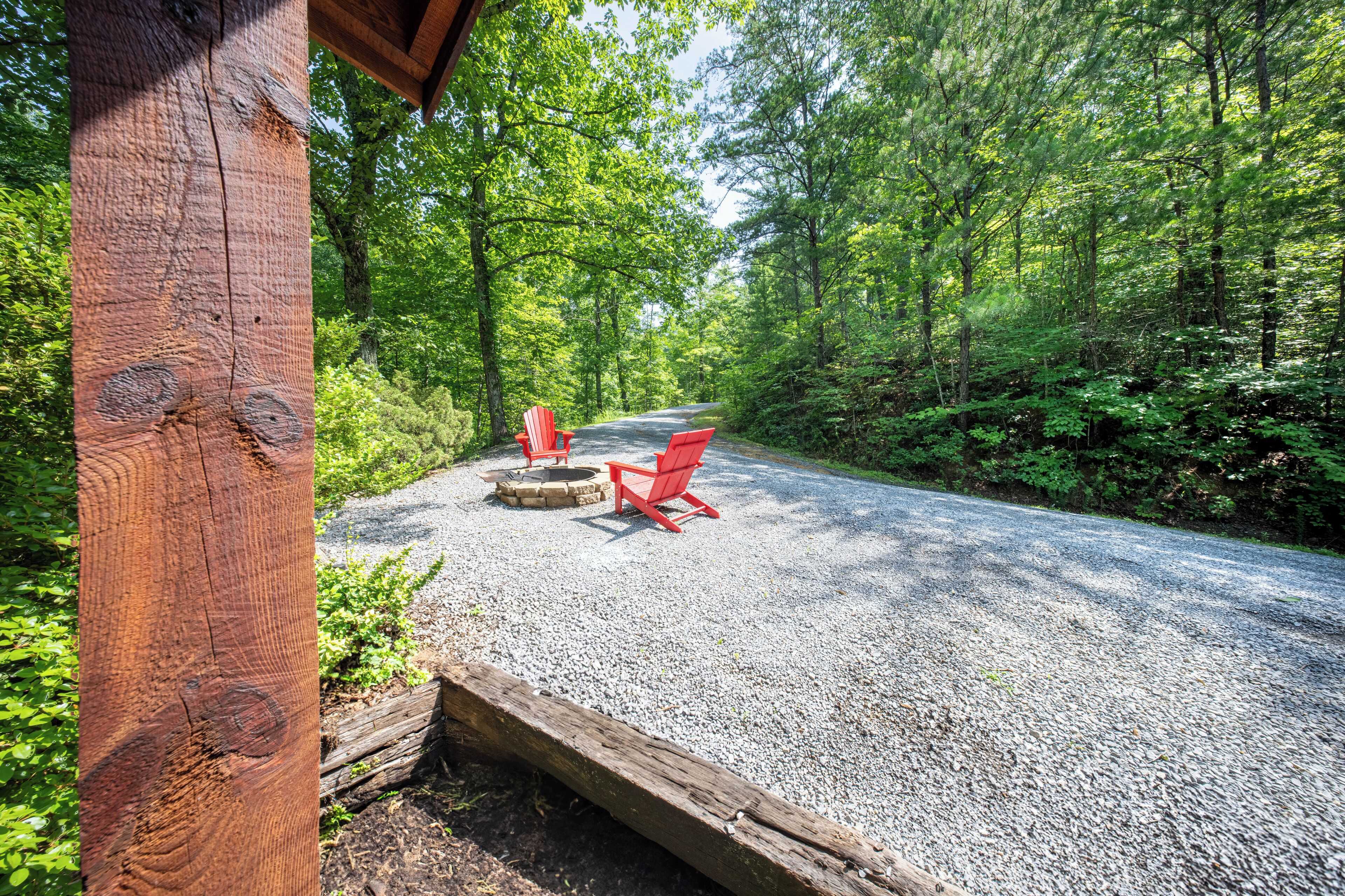 Een grindpad dat door een bebost gebied leidt, met een houten constructie en twee rode Adirondack-stoelen.
