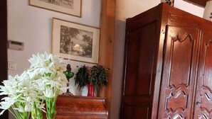 Une pièce avec un fauteuil blanc, un meuble en bois et un vase contenant des fleurs blanches, posé sur une table.
