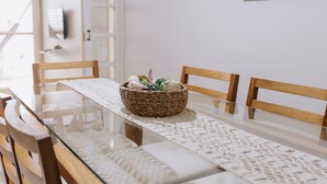 Un comedor con una mesa de vidrio, sillas de madera, una cesta tejida con plantas y un cuadro de peces en la pared.