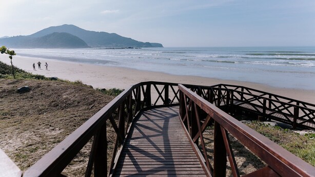 Un paseo marítimo de madera que conduce a una playa, con una montaña al fondo.