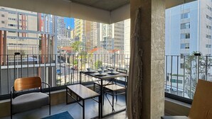 Una habitación moderna con balcón, una mesa de comedor con sillas y un amplio ventanal con vista a la ciudad.